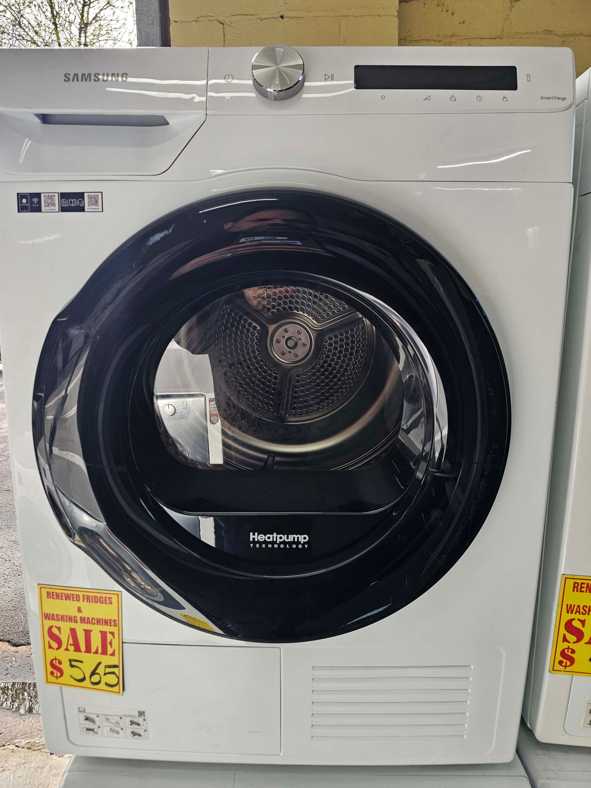 White front-load clothes dryer on display with sale tags, featuring a black circular door.