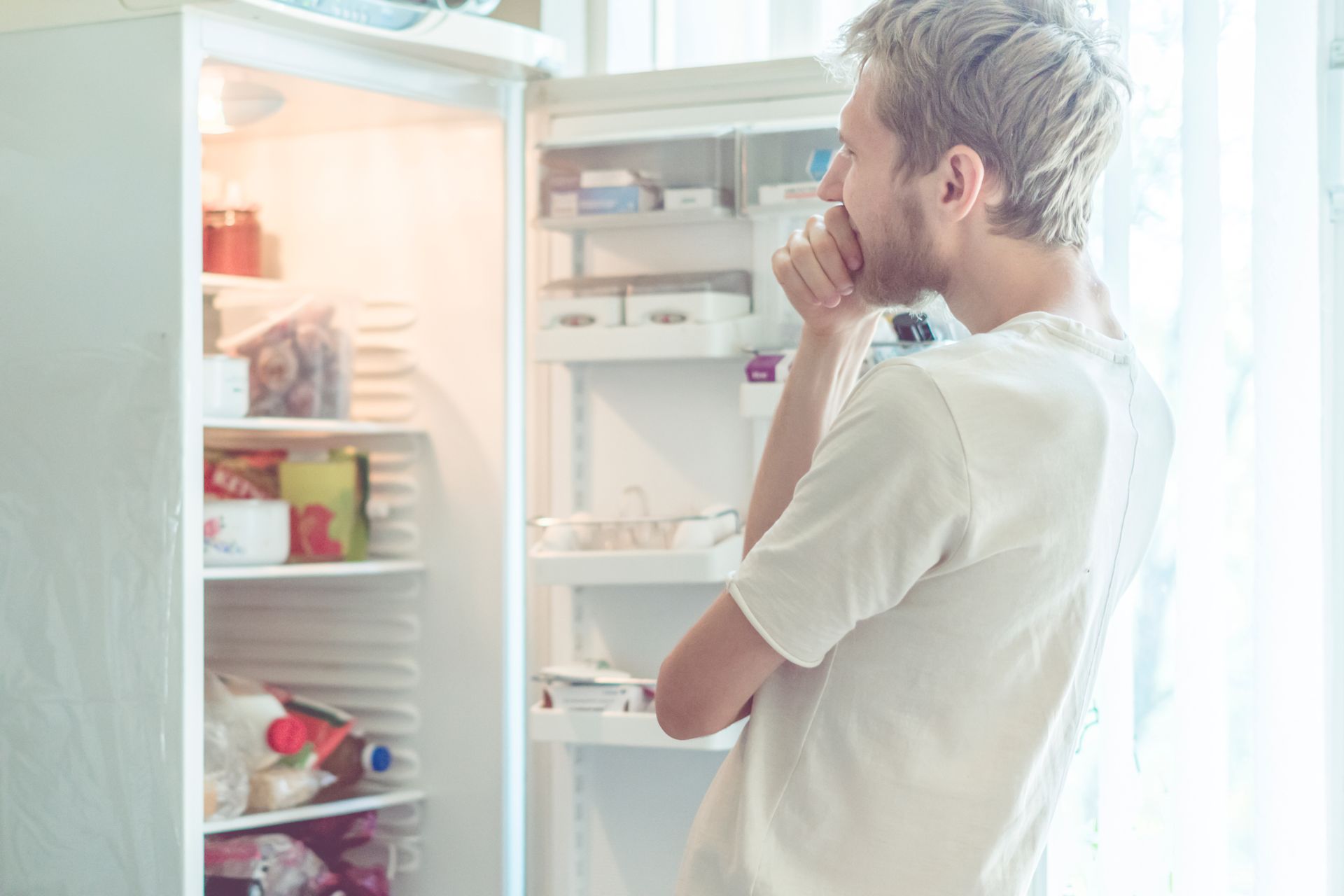 Young man searching for food in the fridge at home.