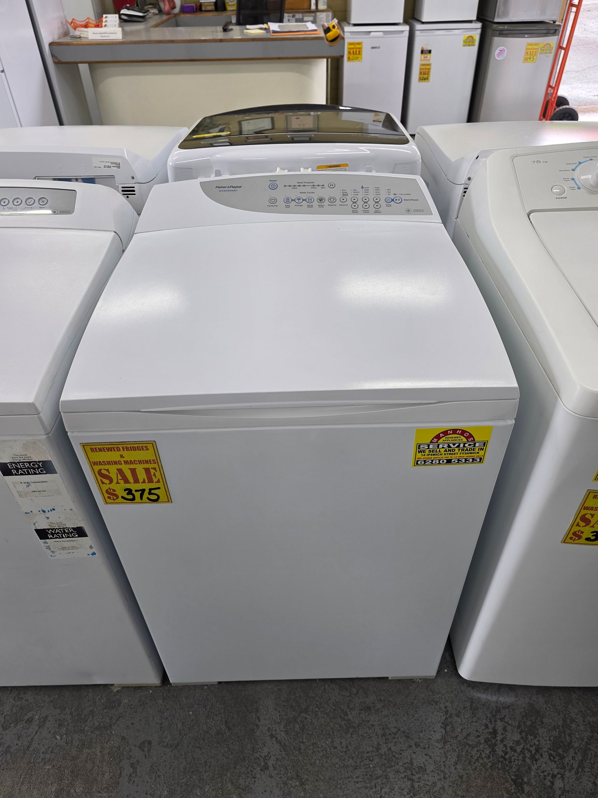 White washing machine on sale. Several similar appliances in a store setting.
