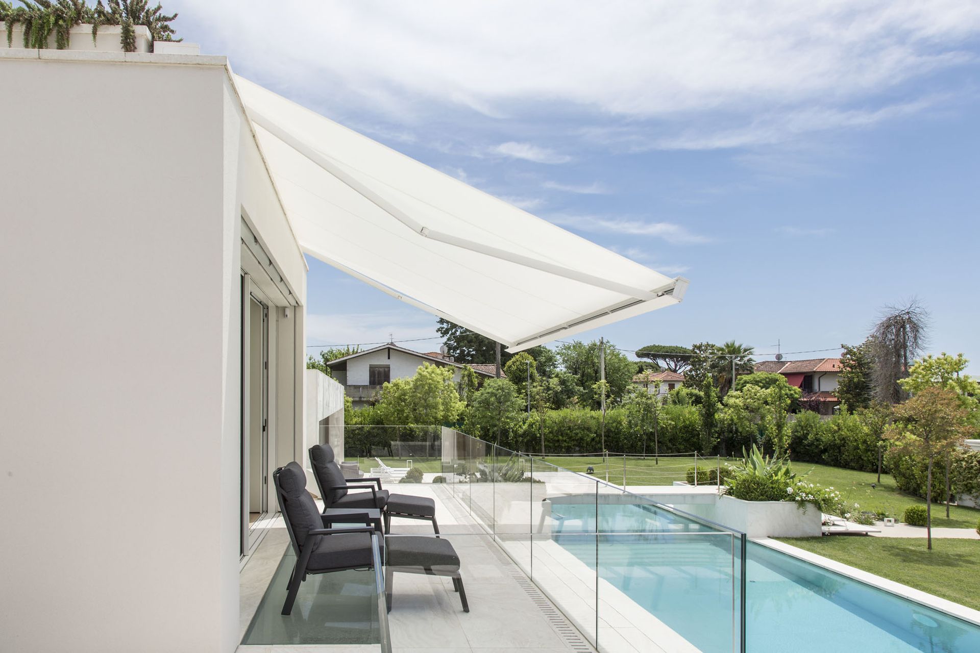 Tenda bianca sopra le sedie a sdraio su un balcone con vista sulla piscina e sul cortile in una giornata di sole.