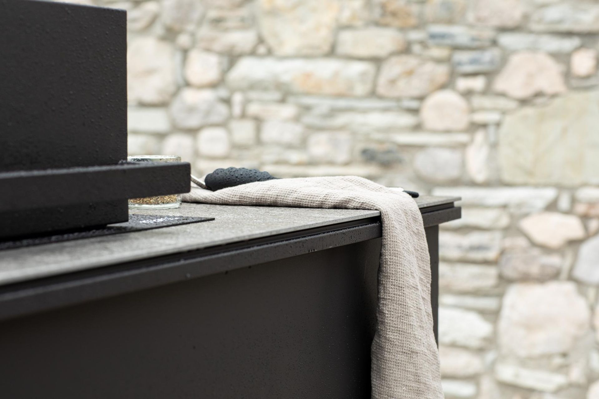 Primo piano di una struttura in metallo nero con un asciugamano chiaro drappeggiato sopra, sullo sfondo un muro di pietra.