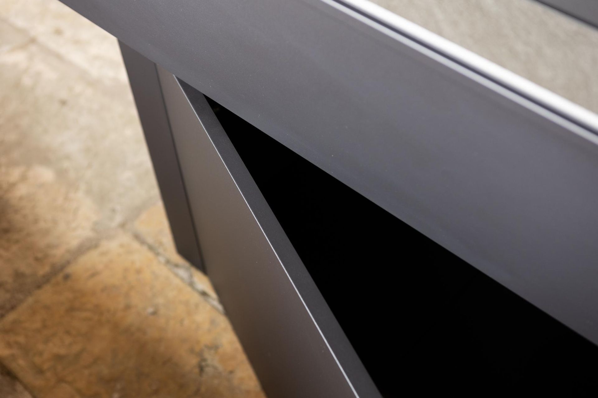 Primo piano di un mobile grigio con un ritaglio triangolare che rivela un interno scuro.
