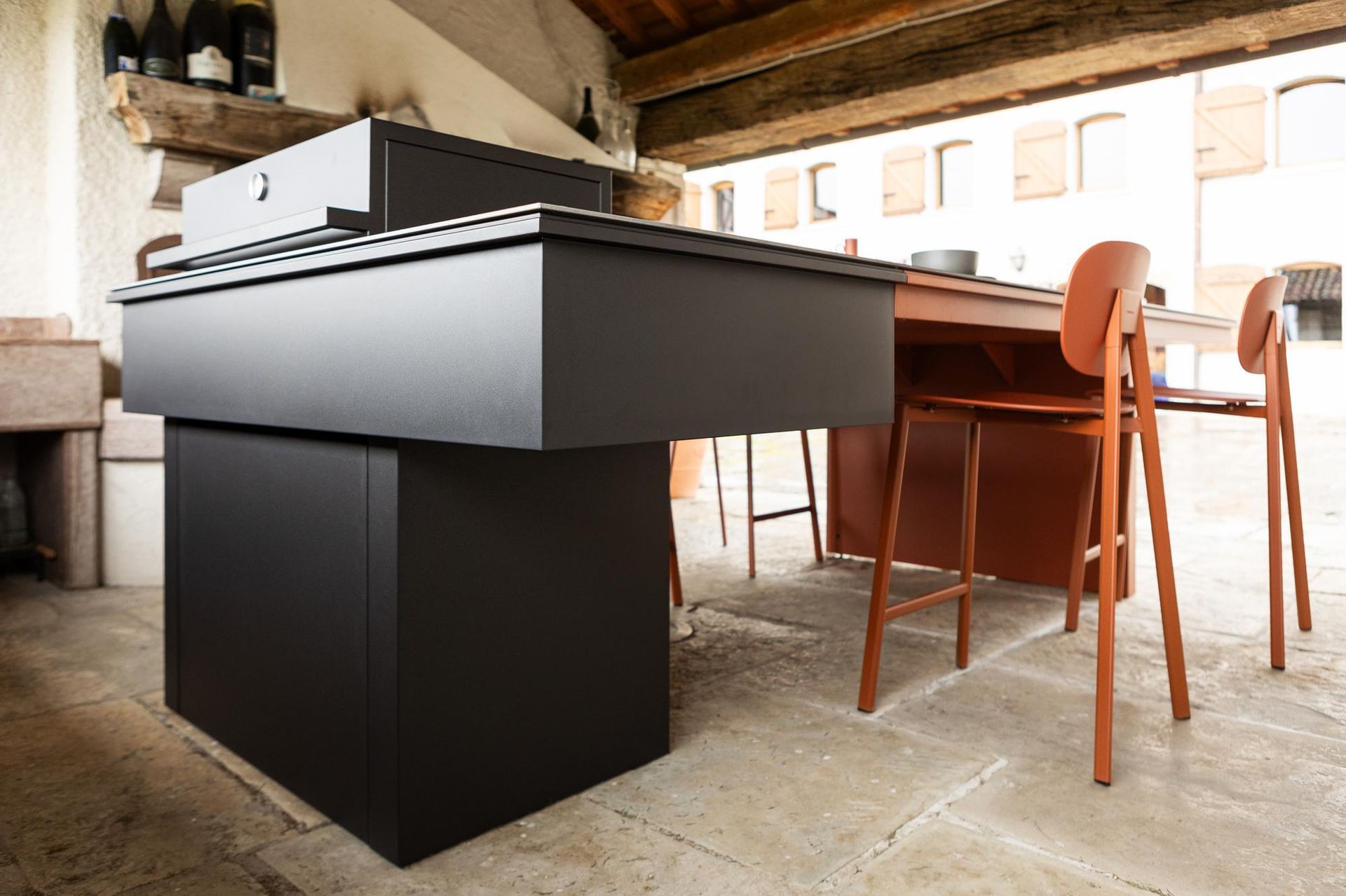 Isola da cucina moderna nera con forme rettangolari, abbinata a sedie e tavolo marroni per esterni.