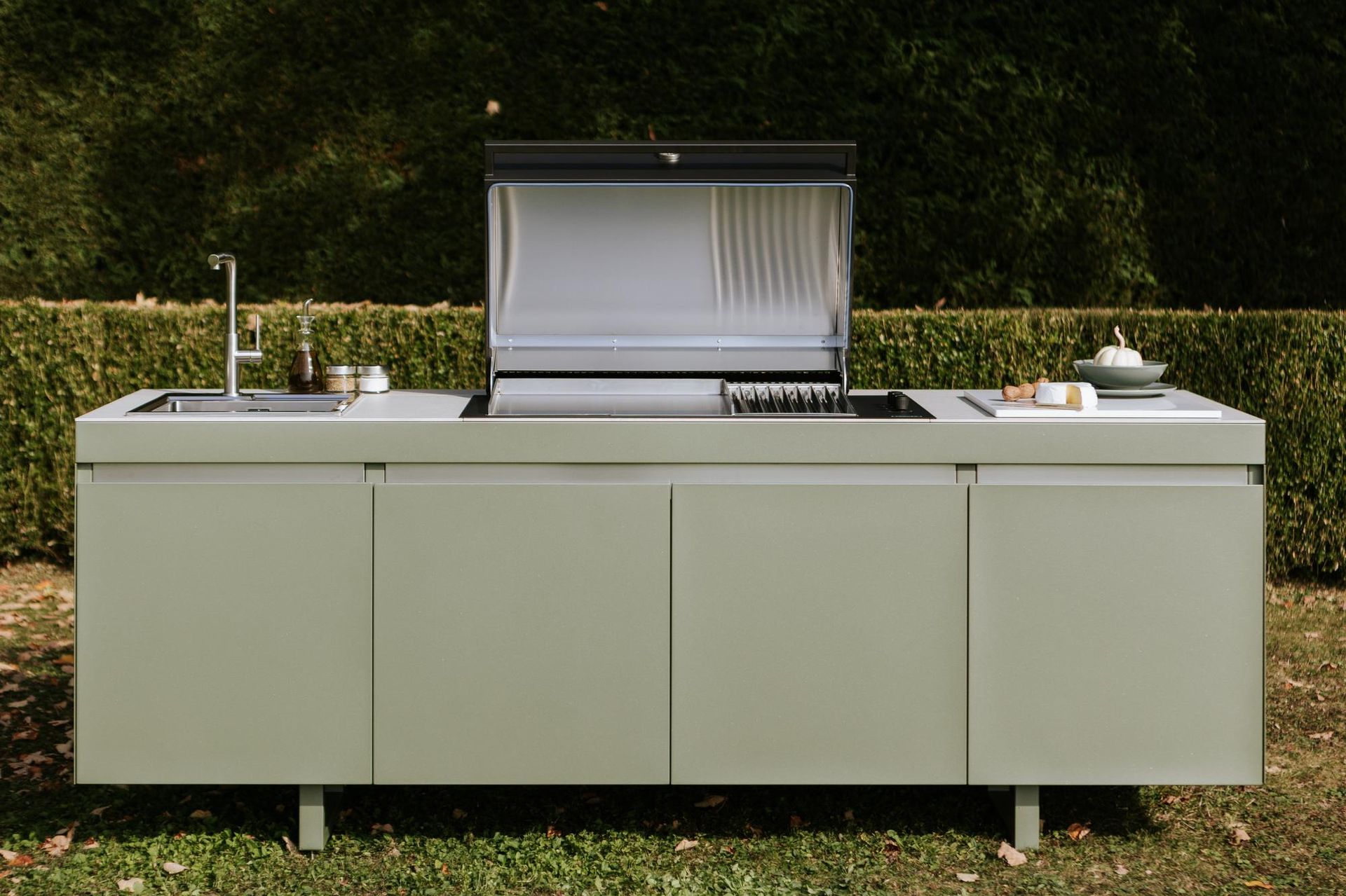 Cucina esterna con lavello, grill e armadietti; finitura verde, situata in un cortile.