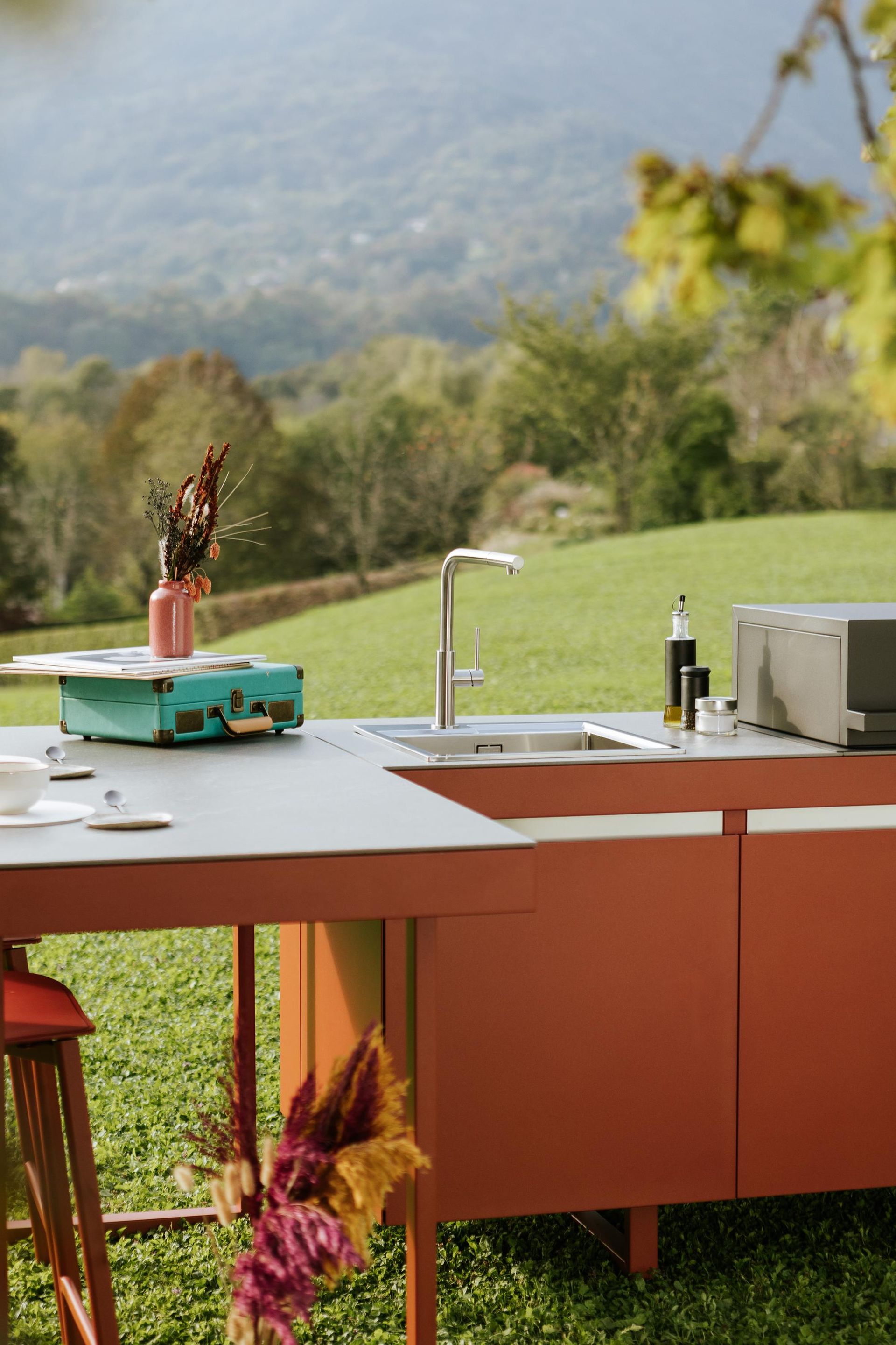 Cucina esterna con lavello, piano di lavoro ed elettrodomestici, situata su una verde collina con vista sulle montagne.
