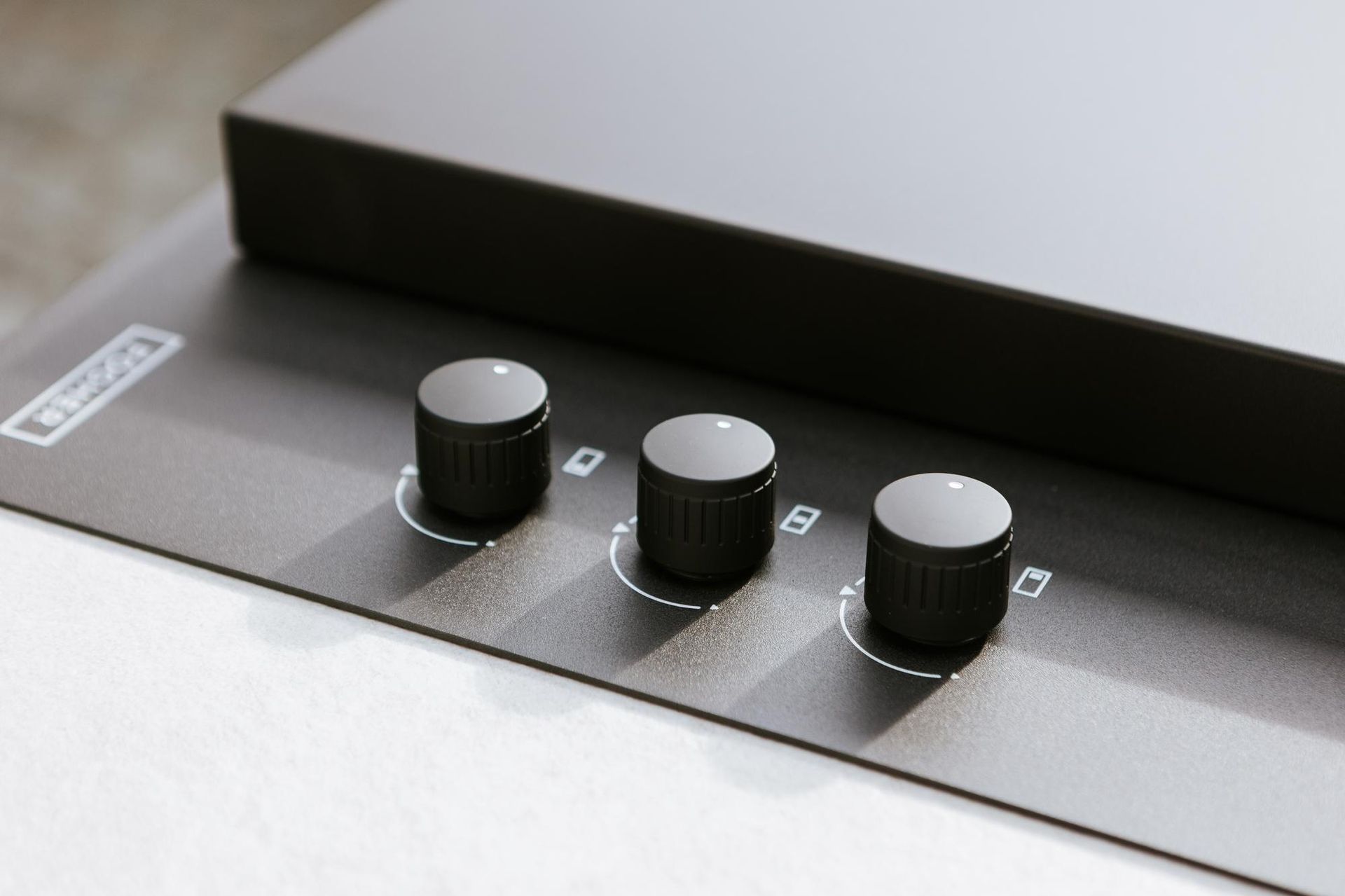 Tre manopole nere su un pannello di controllo grigio scuro, probabilmente per dispositivi audio o elettronici.