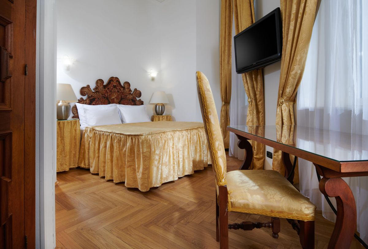 Bedroom with ornate gold bedspread, carved headboard, desk, chair, and TV.