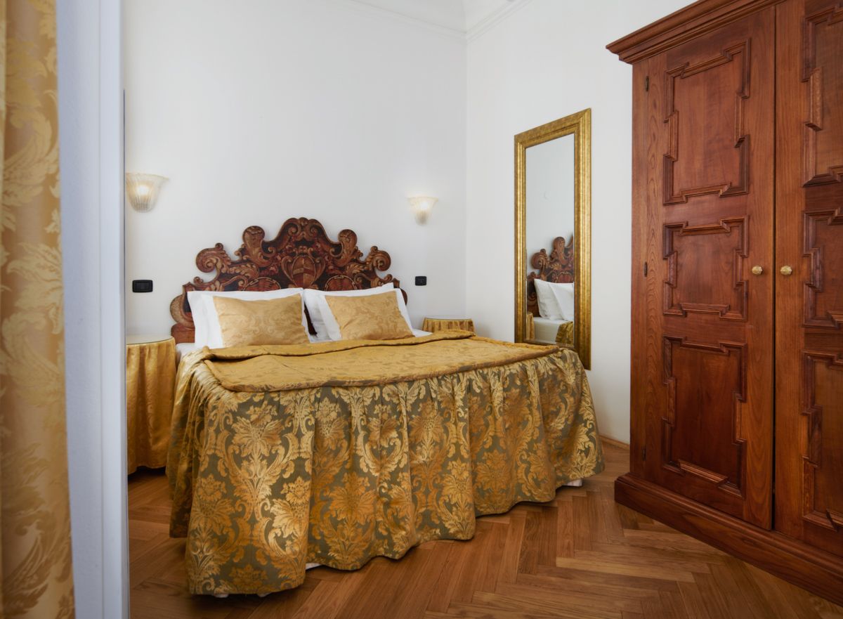 Bedroom with ornate headboard, gold bedspread, wooden wardrobe, and parquet flooring.