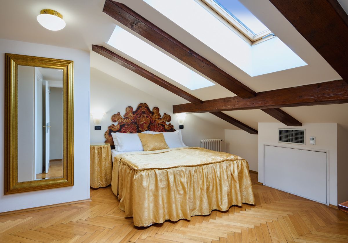 Bedroom with skylights, wooden beams, gold bedspread, large mirror, and ornate headboard.