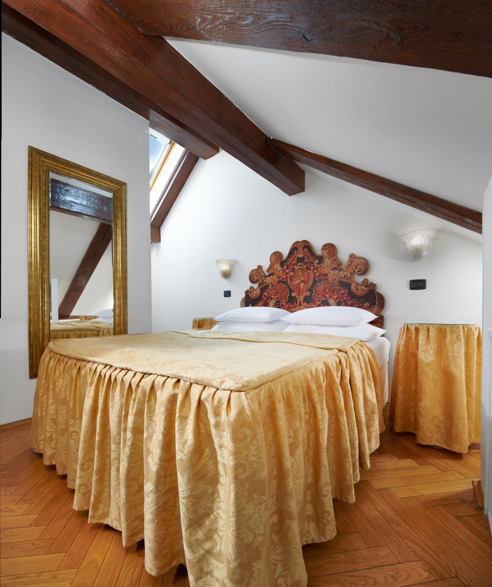 Bedroom with a gold bedspread, large mirror, wooden beams, and a patterned headboard.