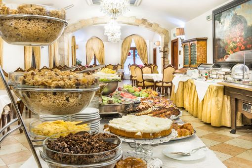 Buffet table laden with food in a dining room with ornate decorations, including a chandelier and painting.