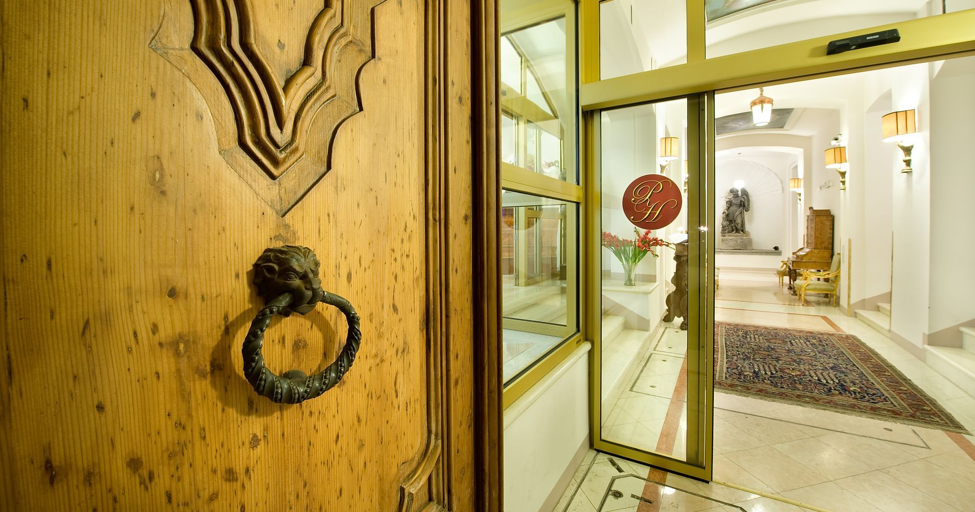 Wooden door with ornate carving and metal knocker, open to a bright hallway.