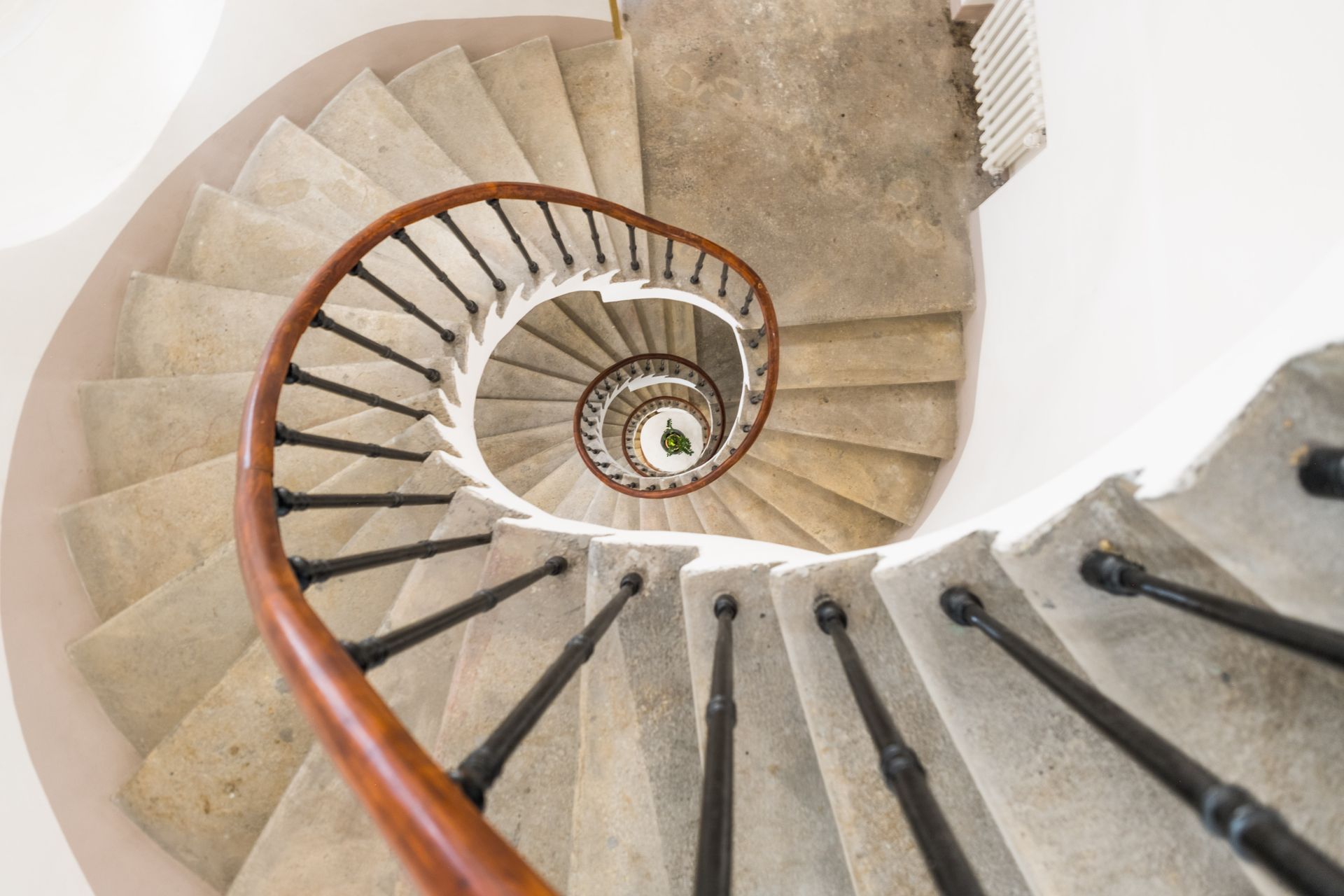 Spiral staircase with stone steps and wooden handrail, viewed from above.