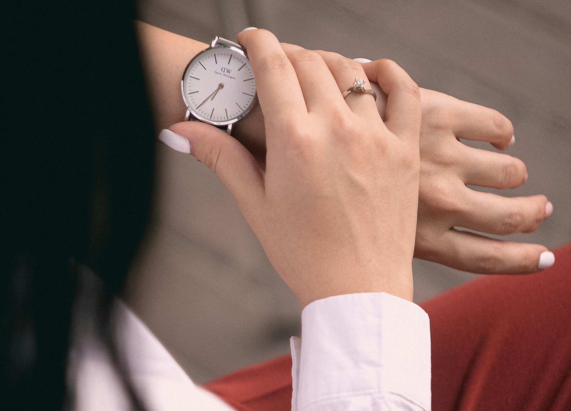 Hand adjusting the strap of a silver wristwatch on a person in a red sweater