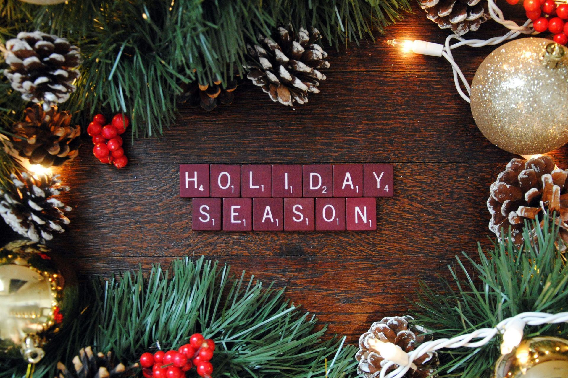 Holiday season text on a rustic wooden background with pine branches, pinecones, and festive ornaments