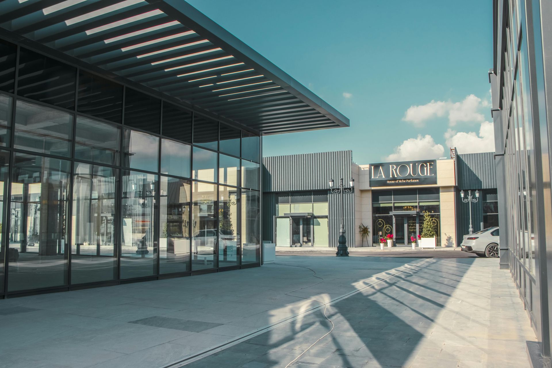 Modern outdoor shopping plaza with glass storefronts and a shaded walkway under a clear blue sky