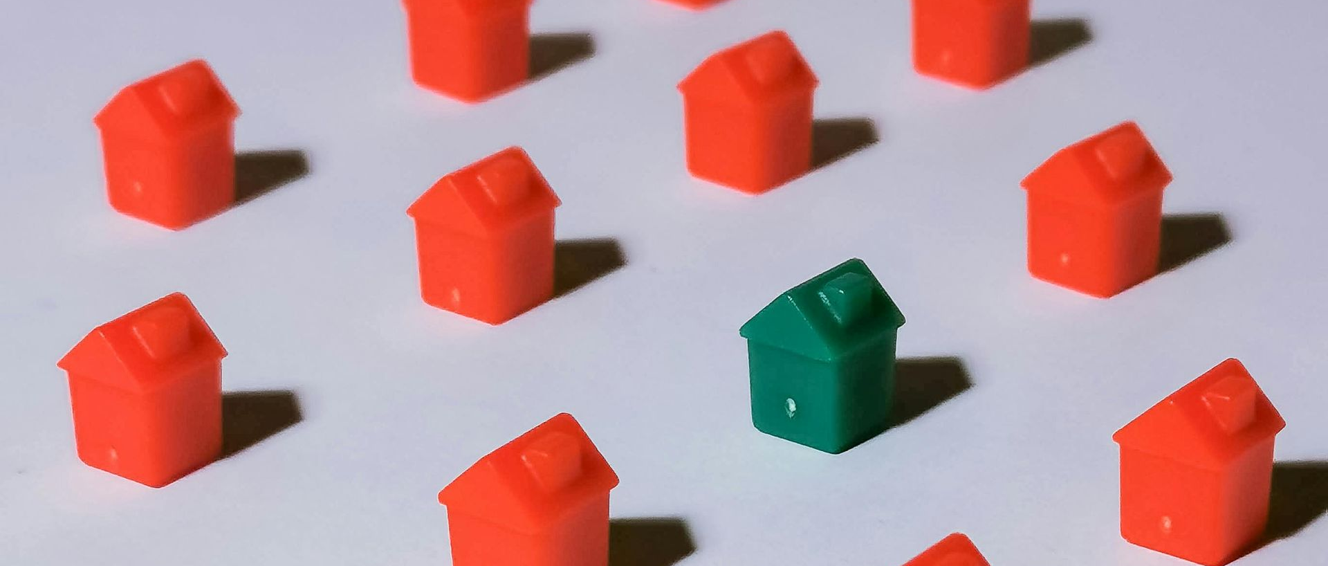 Small red house models with one green house on a white surface, casting shadows.