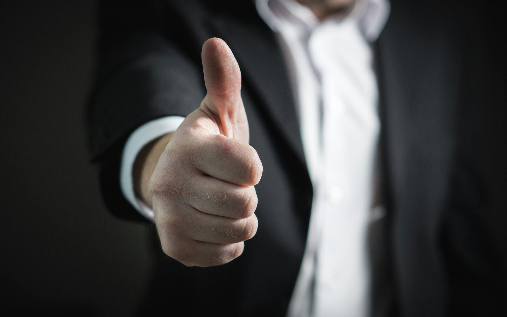 Hand in a dark suit giving a thumbs-up gesture against a black background