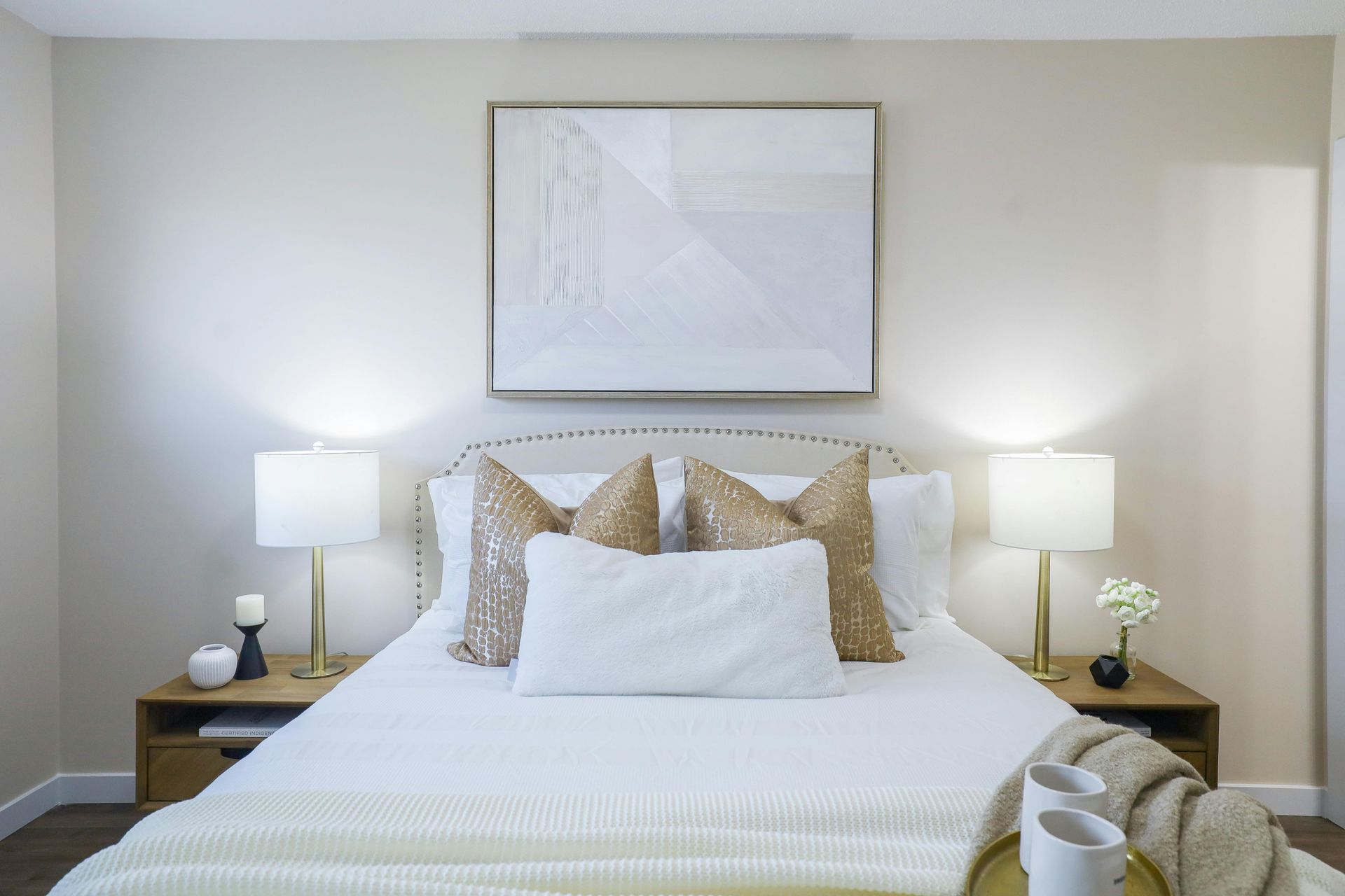 Bright bedroom with a neatly made bed, bedside lamps, and framed art above the headboard