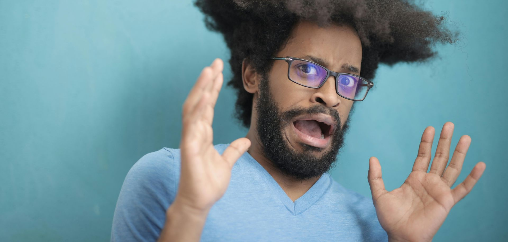 Man with glasses and raised hands speaking against a blue background