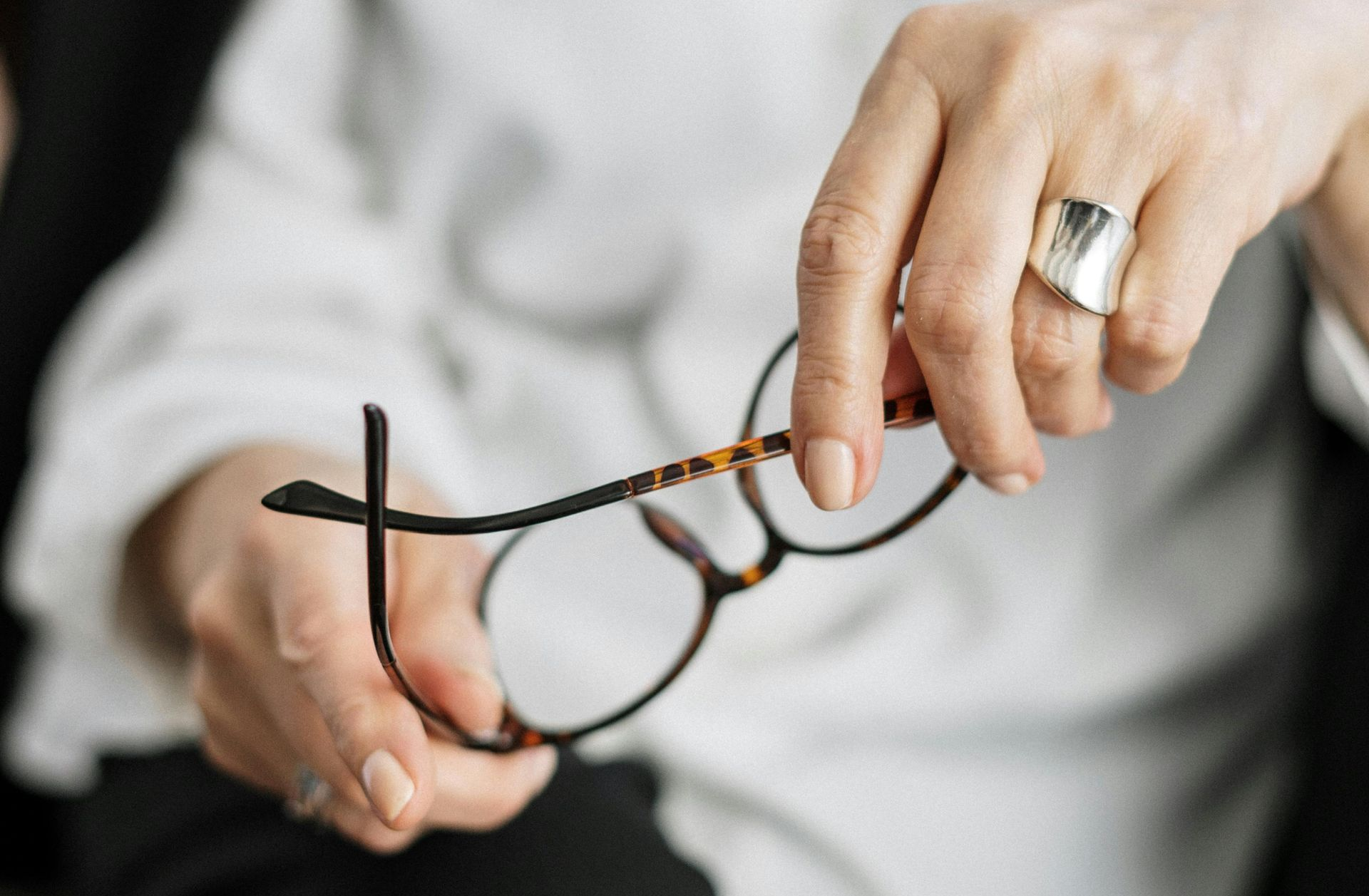 Hands adjusting tortoiseshell eyeglasses on a white-clad lap