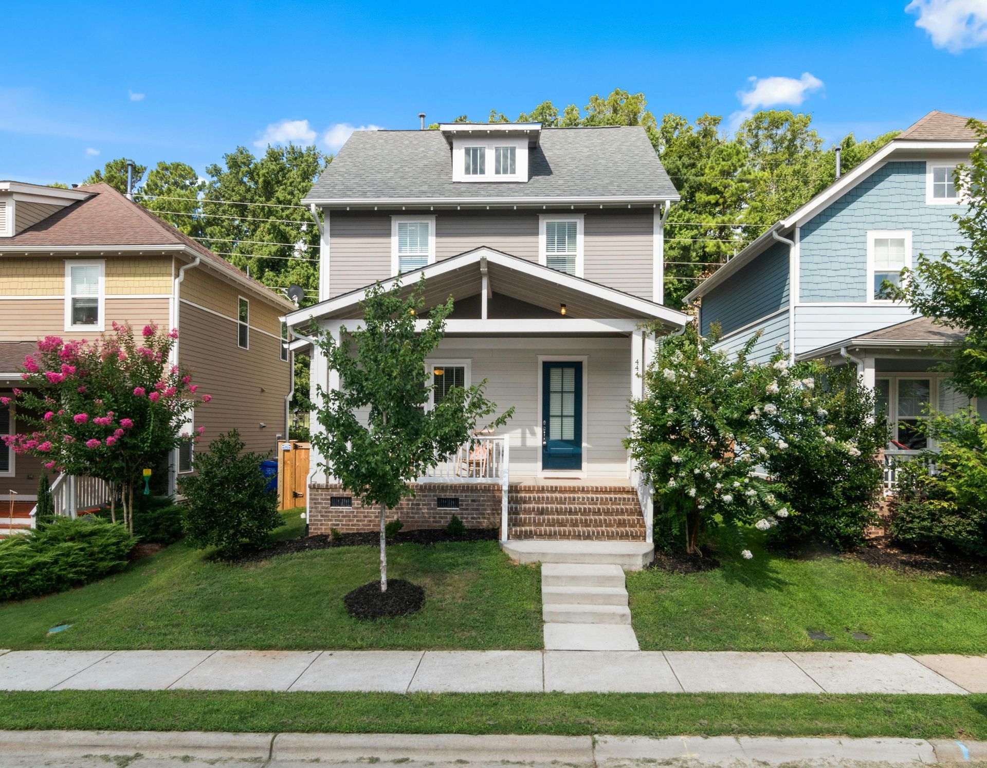 Front view of a gray two-story house with a small porch, steps, and a green lawn