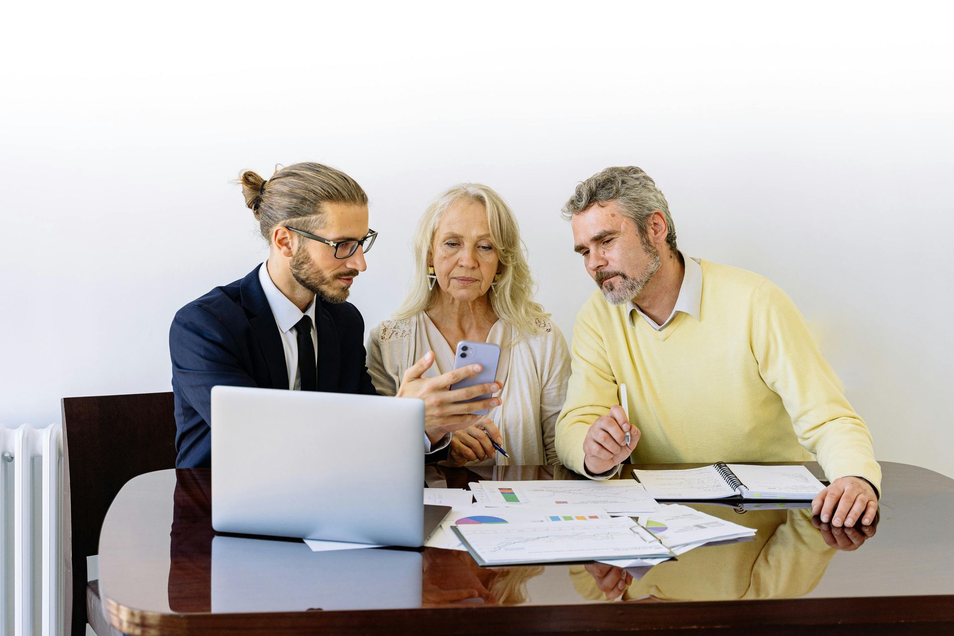 Three people in a meeting reviewing charts beside a laptop at a desk