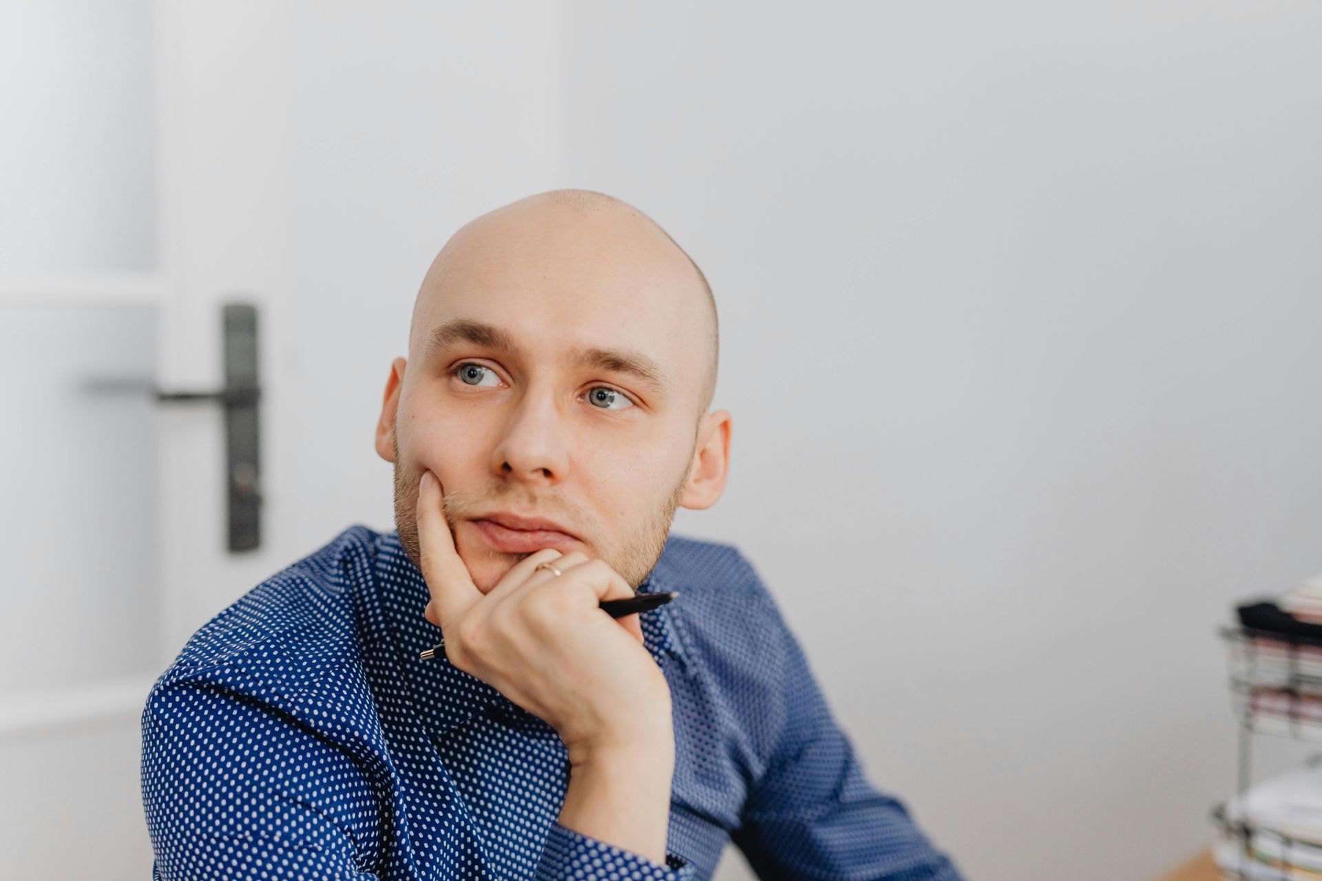 Man resting chin on hand, looking thoughtfully off-camera in a bright room