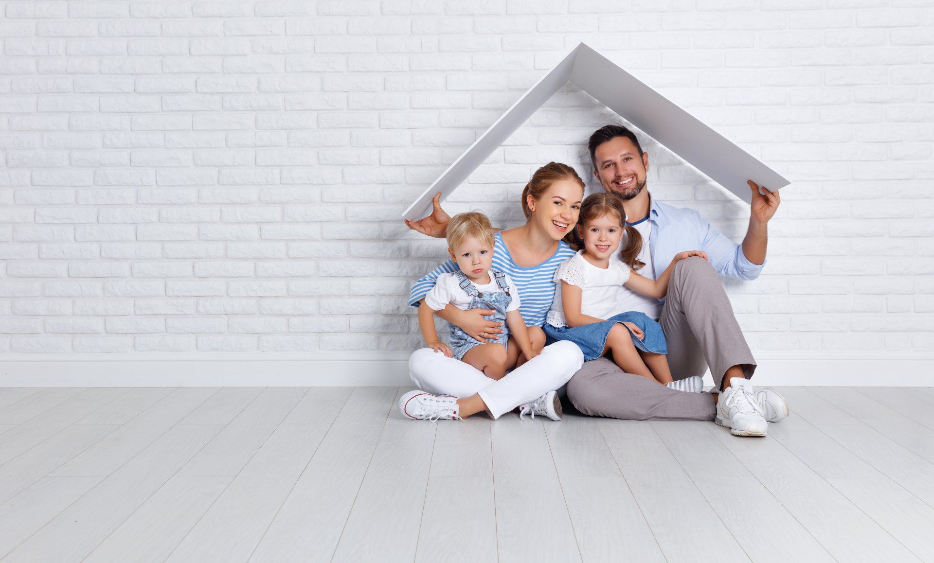 Family sitting together under a small house-shaped frame on a white floor, smiling in a bright room