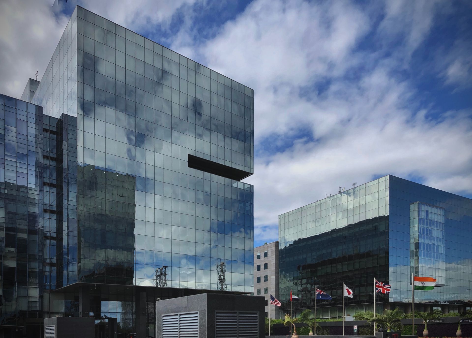 Modern glass office buildings reflecting clouds under a blue sky, with flags in front.