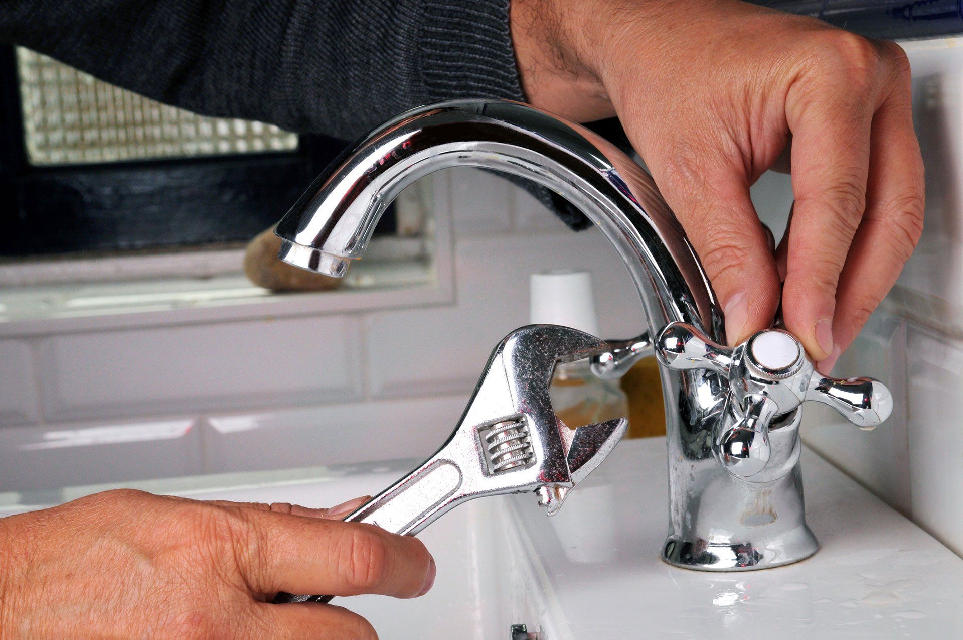 plumbing service technician tightening faucet with wrench