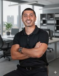 Smiling Tolga Terzioglu in a black polo stands with arms crossed in a modern office.