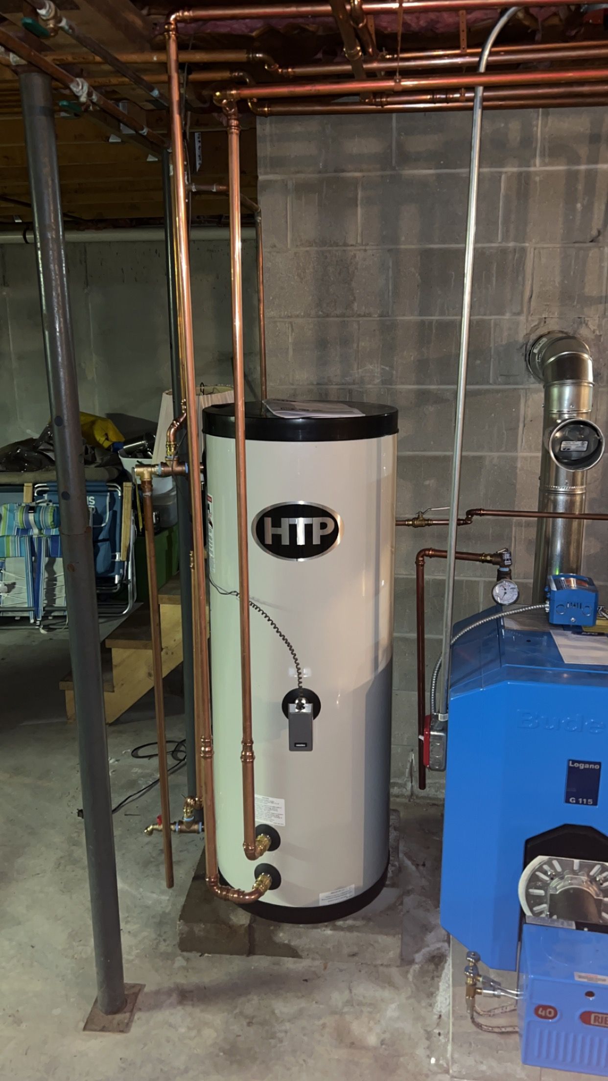 A cylindrical water heater with copper pipes in a basement setting.