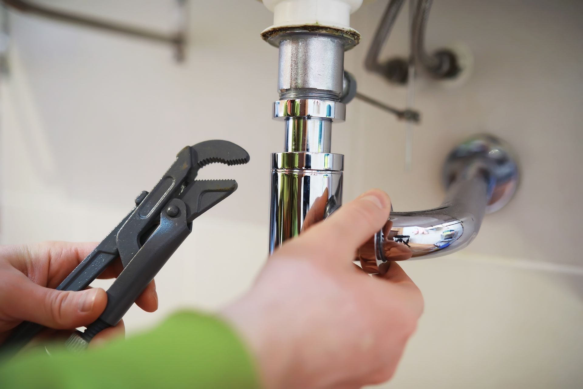 A person is fixing a sink pipe with a wrench.