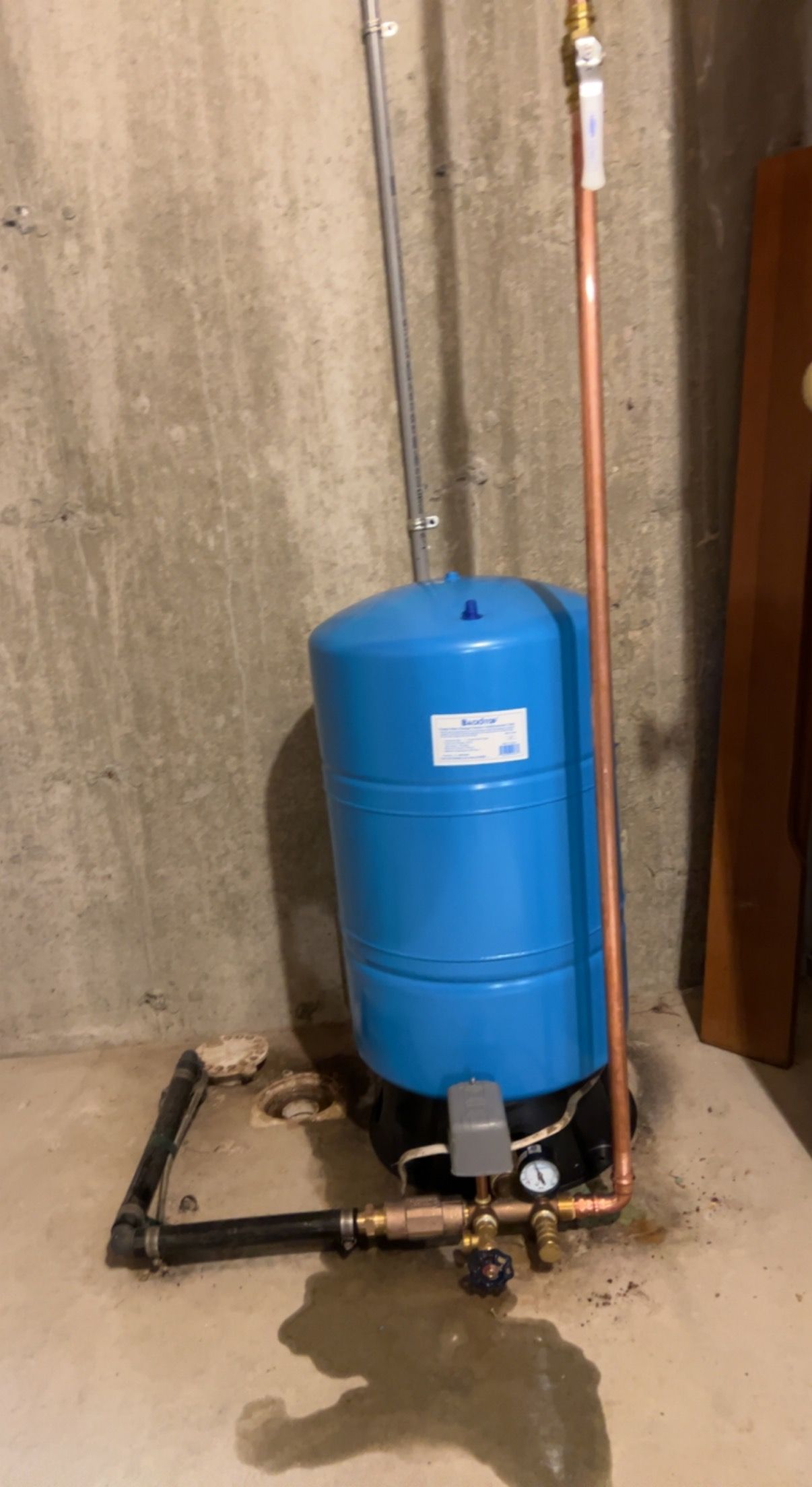 A blue water tank is sitting next to a copper pipe in a basement.