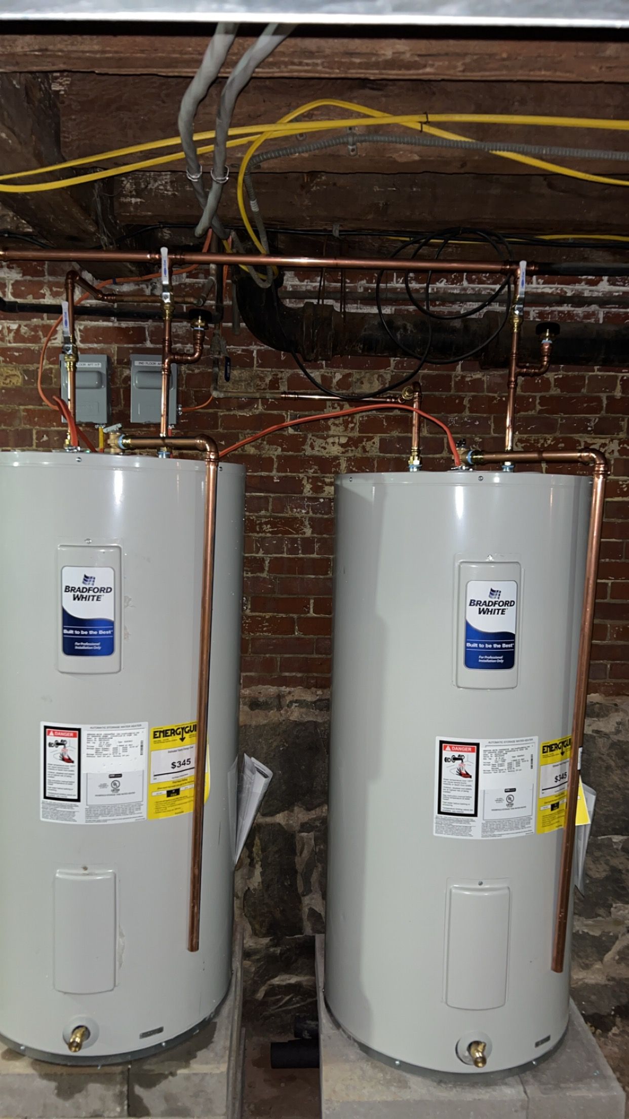 Two water heaters are sitting next to each other in a basement.