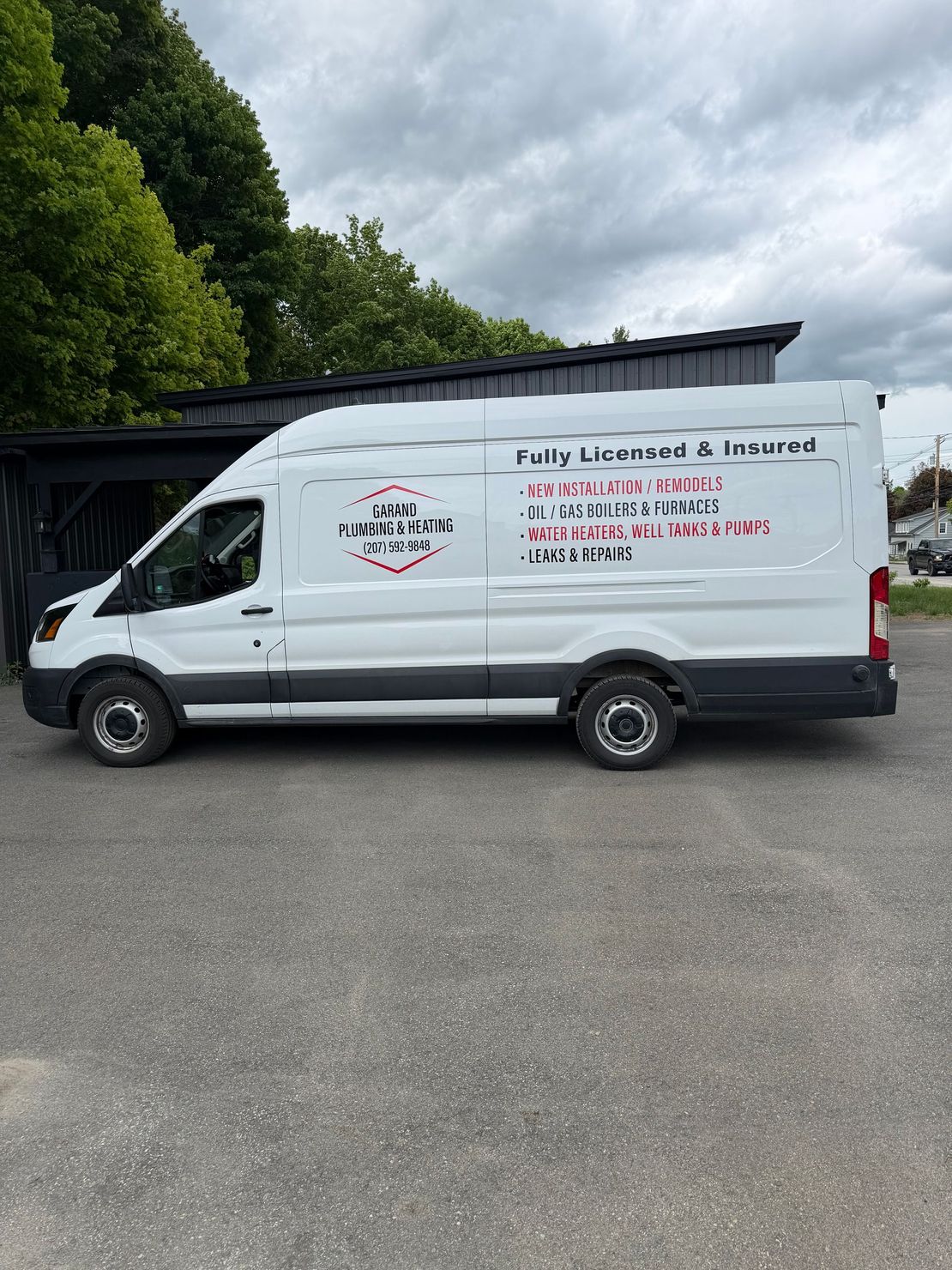 White cargo van with company lettering parked outdoors on a paved lot, trees and cloudy sky behind.