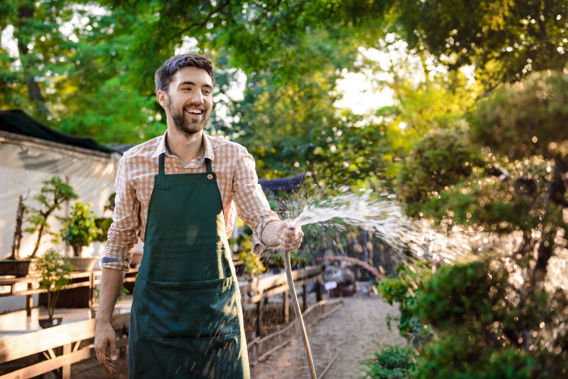 A man is watering plants with a hose in a garden.