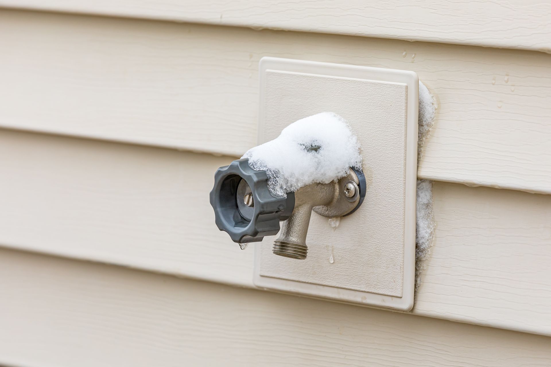 Frost-covered outdoor water spigot mounted on beige siding