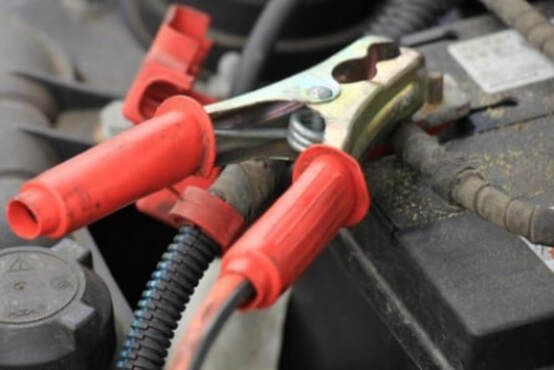 A close up of a car battery with red clamps attached to it