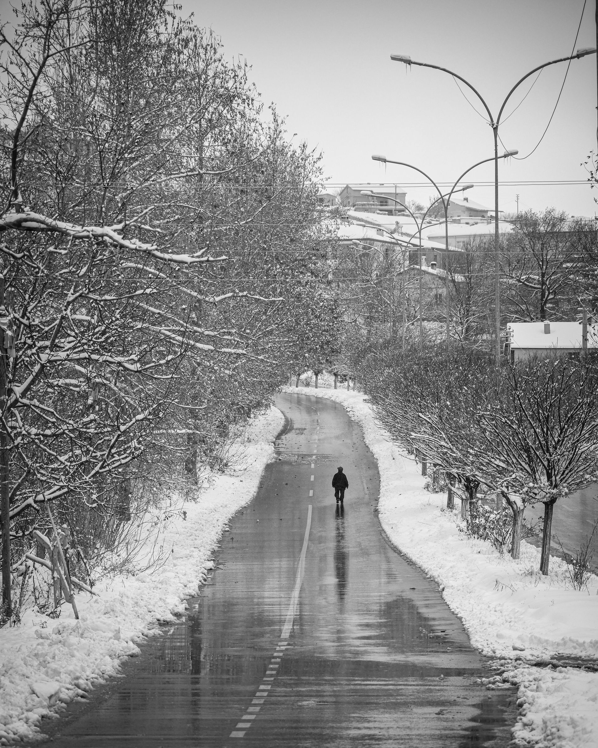 A black and white photo of a person walking down a snowy road