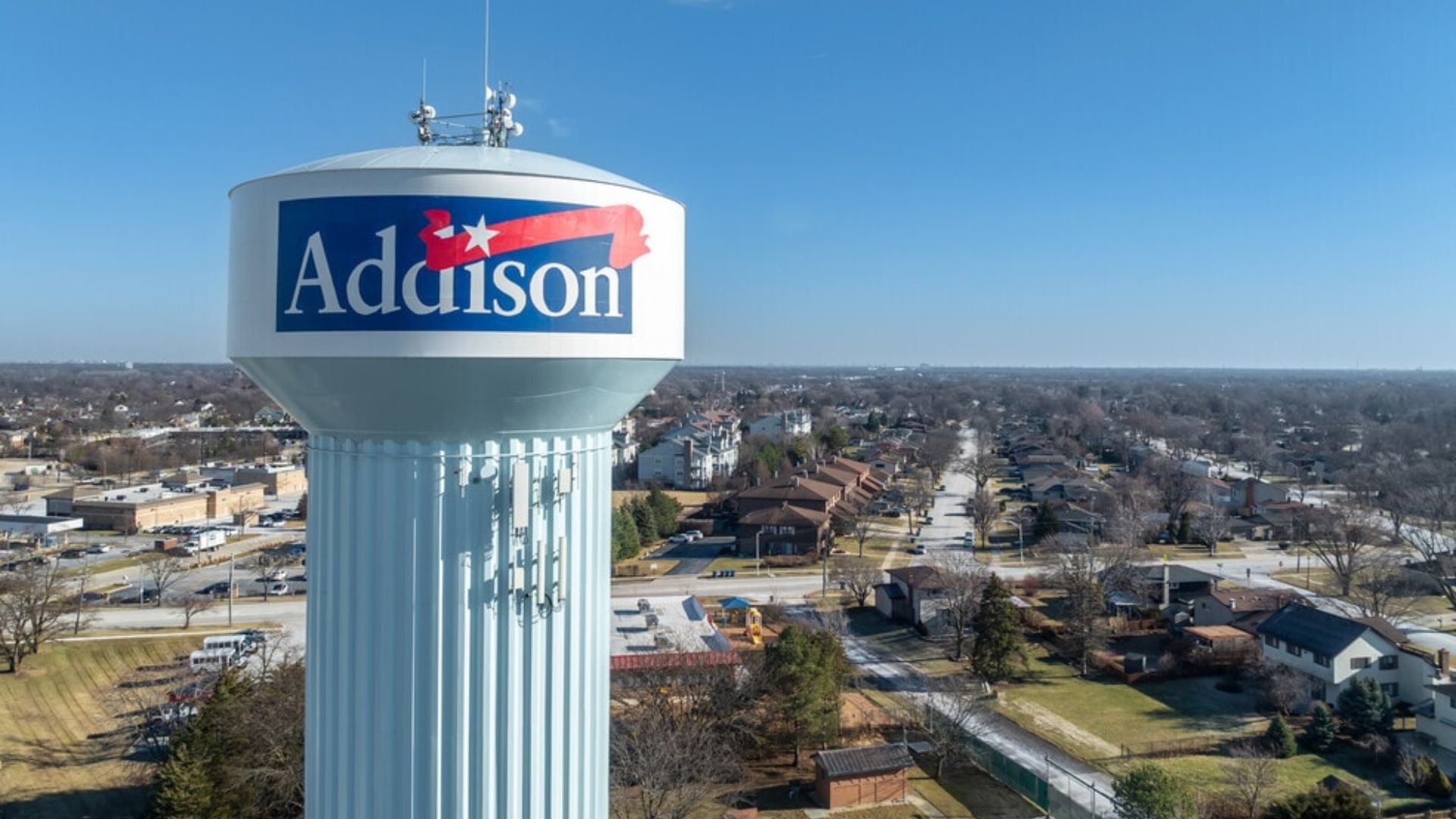 Addison water tower with blue logo above a suburban neighborhood under a clear sky