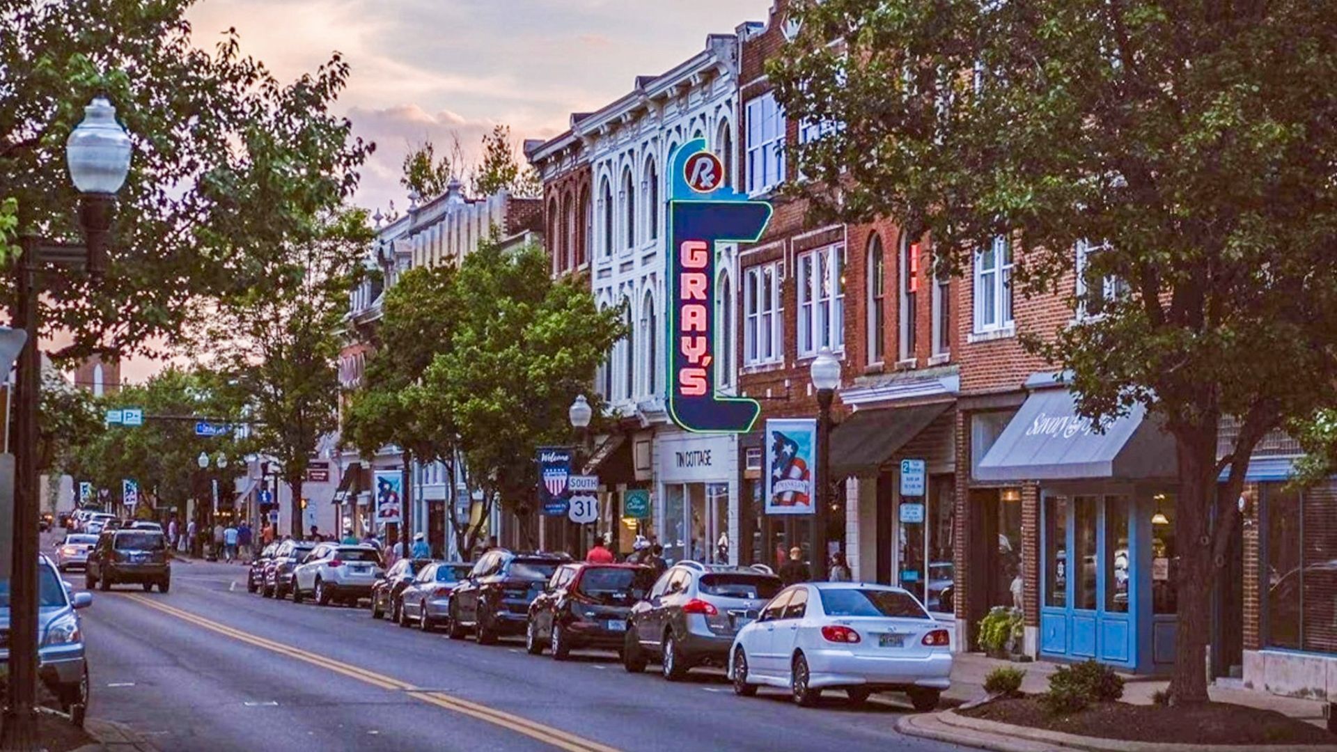 Tree-lined downtown street with parked cars and brick storefronts, including a blue “JONES” sign.