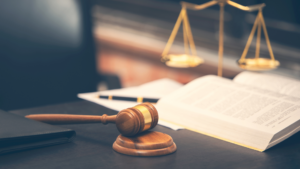 Gavel on a desk beside an open law book and scales of justice in warm light