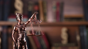 Bronze Lady Justice statue holding scales in front of a blurred bookshelf background