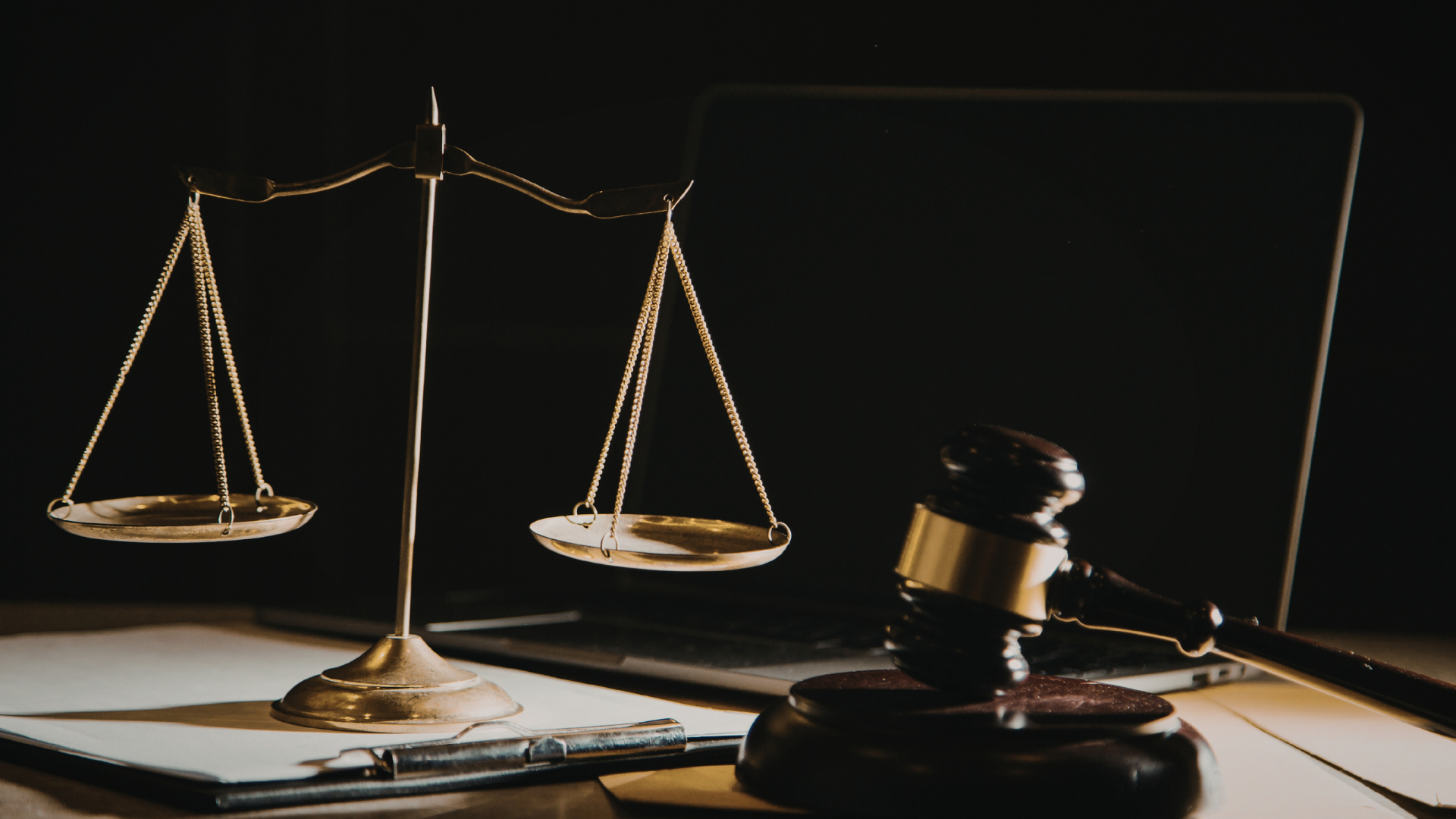 Law book, balance scales, and gavel on a desk in a dimly lit legal setting