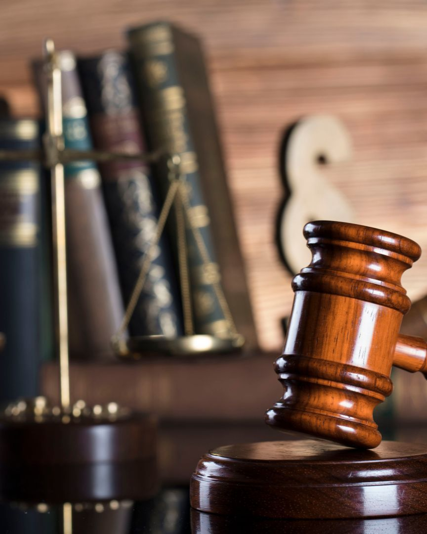 Wooden judge’s gavel resting on a desk with law books in the background.