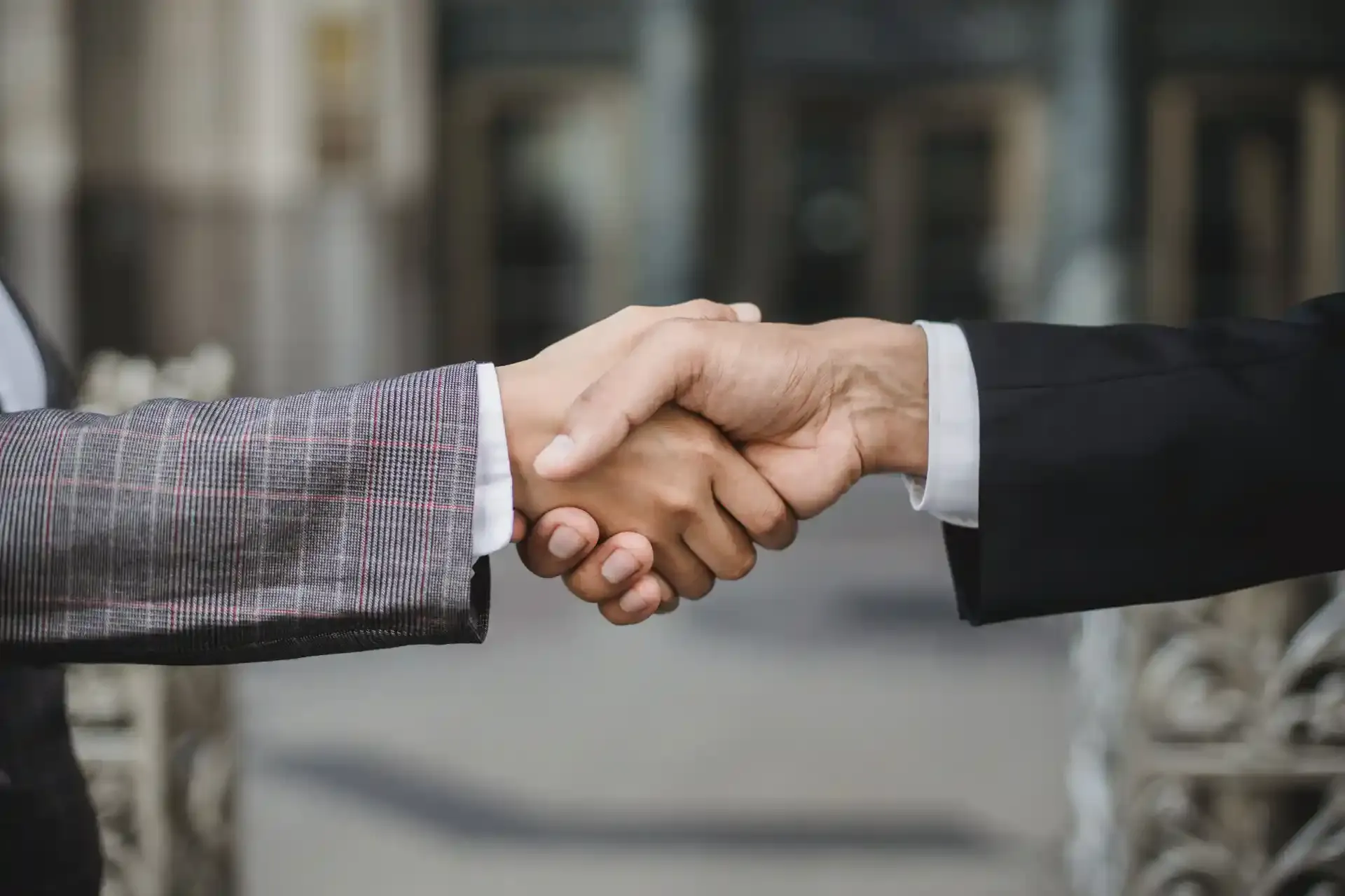 Two people in business suits shaking hands outdoors, symbolizing agreement