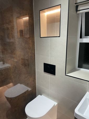 Modern bathroom with toilet, recessed shelf, and window, featuring neutral-toned tiles and black accents.