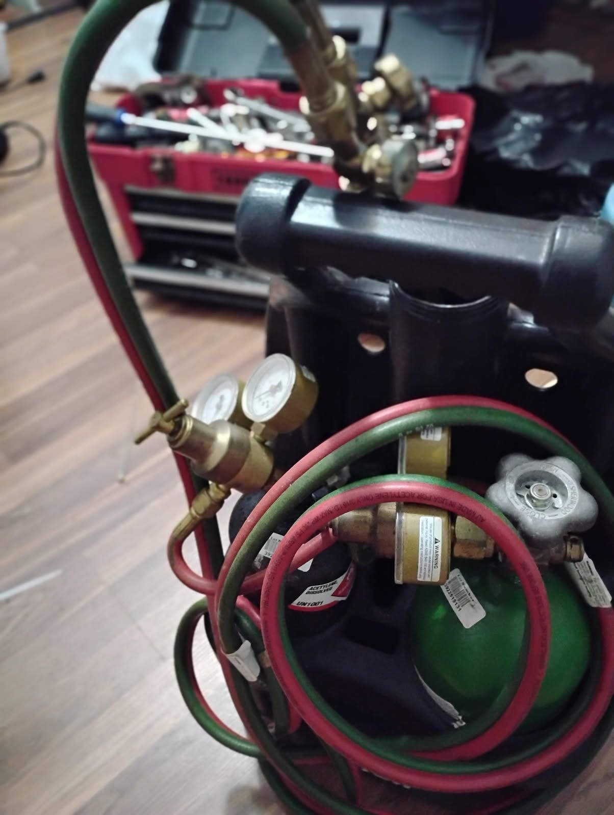 Close-up of a red and green mechanical assembly with hoses, valves, and wires on a workbench